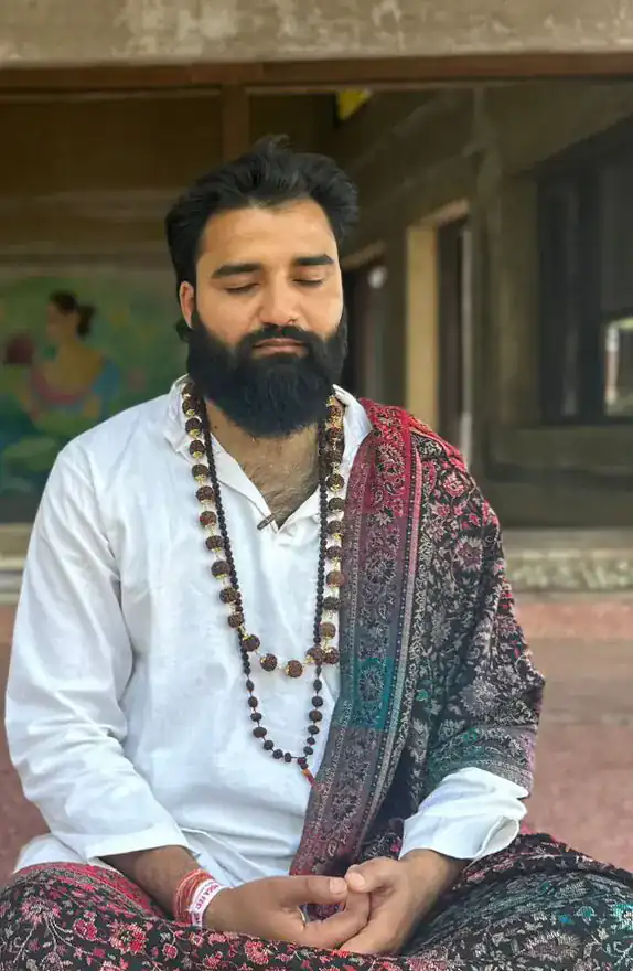 Yogi Arya meditating with eyes closed on a temple step, wearing a long mala and a paisley shawl