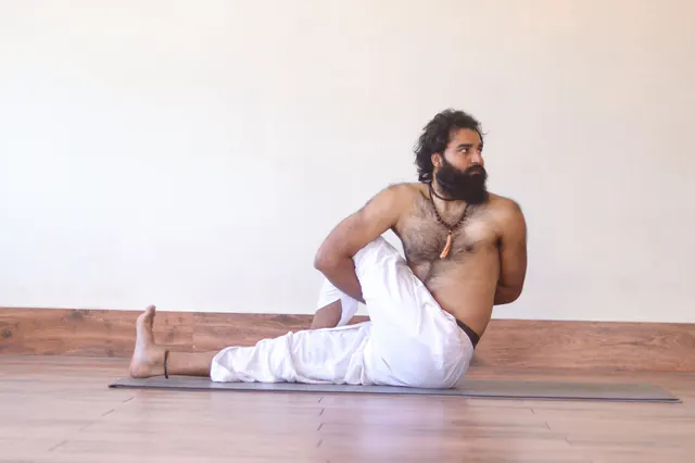 Yogi Arya in a seated spinal twist in a quiet yoga hall