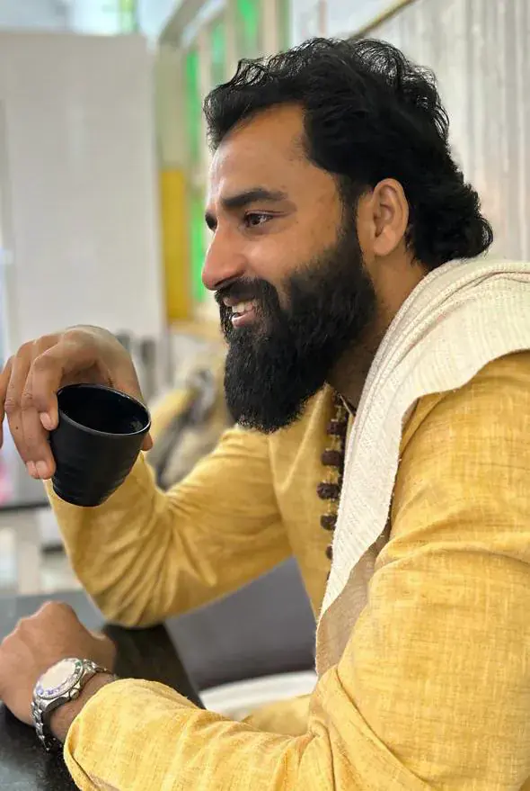 Yogi Arya laughing in profile while holding a cup of tea