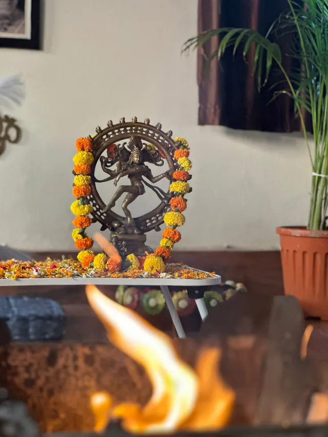 A brass Nataraja statue in a ring of flames, decorated with marigold garlands