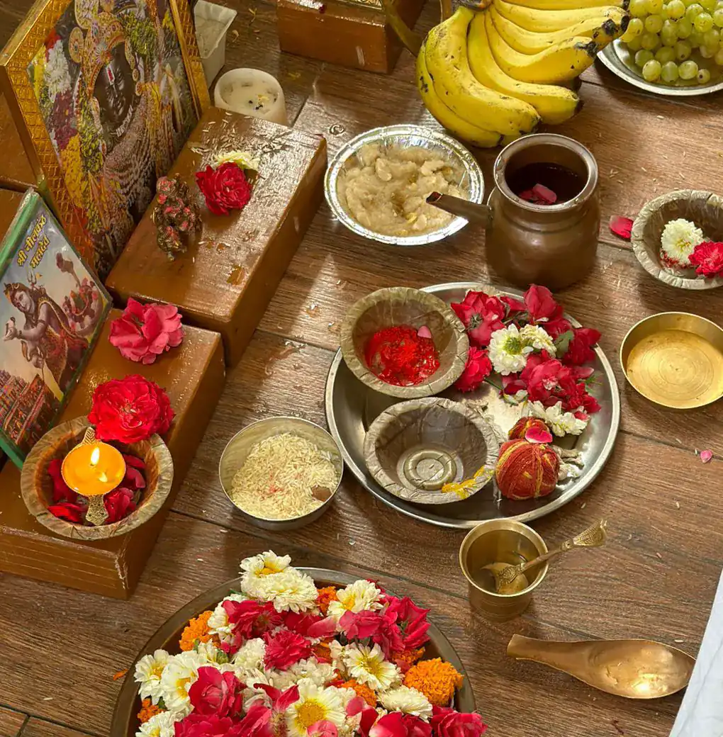 An overhead view of a puja offering with flowers, fruit, a lamp and brass bowls
