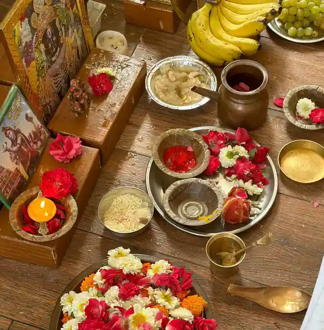 An overhead view of a puja offering with flowers, fruit, a lamp and brass bowls